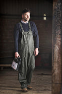Man wearing green overalls holding a tool box in a dimly lit room.