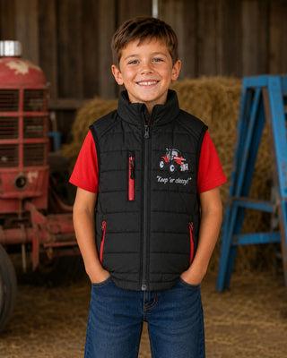 Boy wearing a black padded tractor gilet with red zips and matching red T-shirt on a farm.
