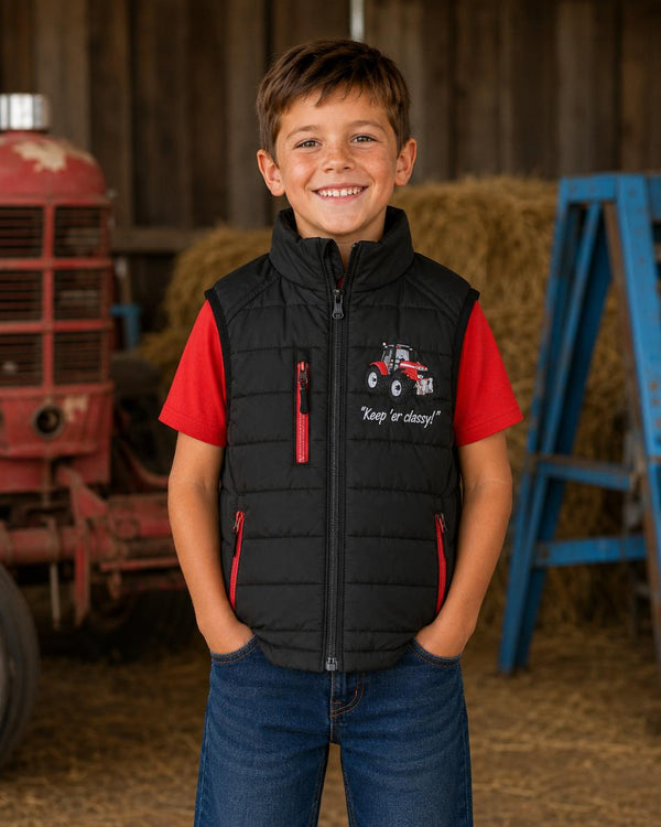 Boy wearing a black padded tractor gilet with red zips and matching red T-shirt on a farm.