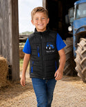 Boy walking through a farmyard wearing a black tractor bodywarmer with blue zip details.