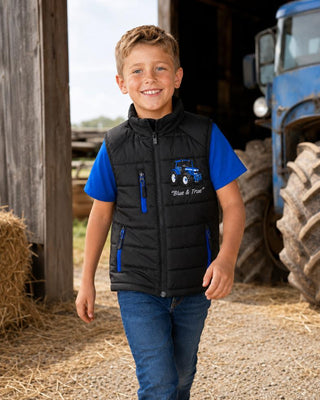 Boy walking through a farmyard wearing a black tractor bodywarmer with blue zip details.