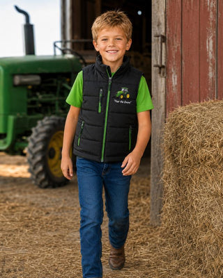 Boy walking beside a green tractor wearing a black bodywarmer with green zips and T-shirt.