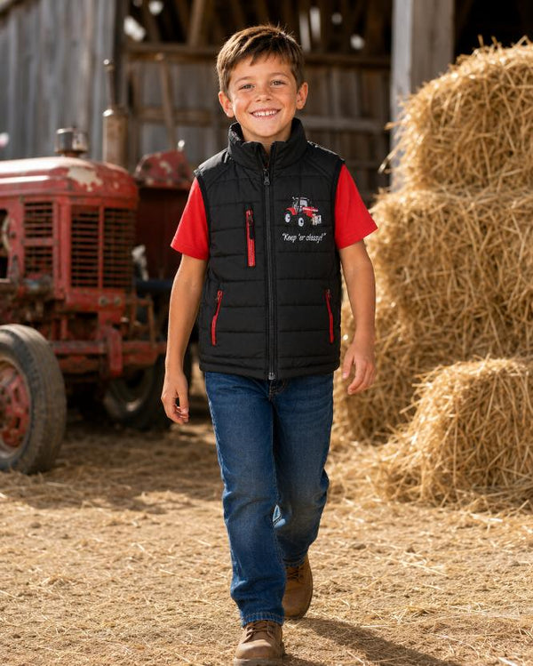 Boy walking on a farm wearing a black tractor bodywarmer with red zips and a red T-shirt
