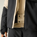 Close-up of a person wearing a black and beige color-blocked jacket, showing the front zipper, snap-button placket, and fabric texture.