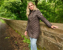 Woman wearing Lighthouse Laurel Cocoa coat outdoors beside a stone wall
