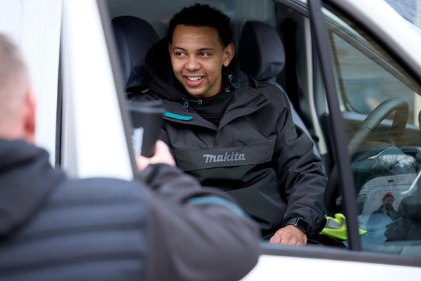 Person in a Makita jacket interacting with another person outside a vehicle.