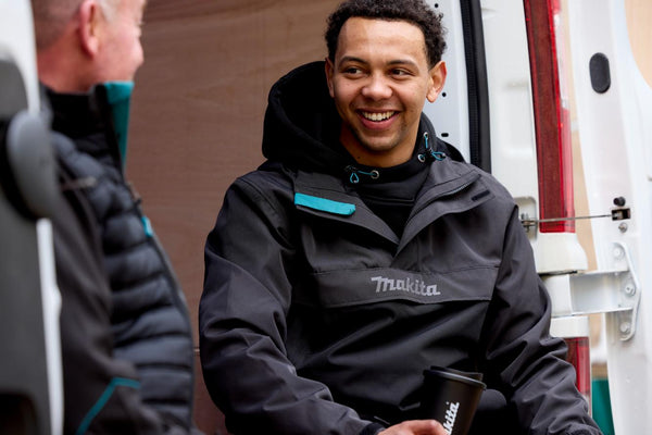 Person wearing a Makita jacket sitting next to a vehicle
