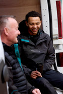 Two men sitting next to a van, one wearing a Makita Aero work jacket.