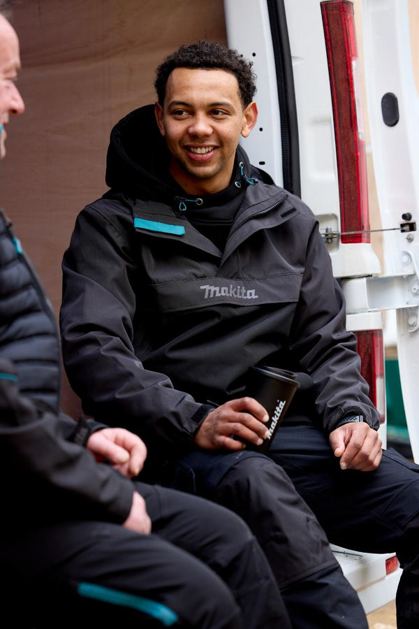 Two men sitting next to a van, one wearing a black jacket with 'Makita' branding.