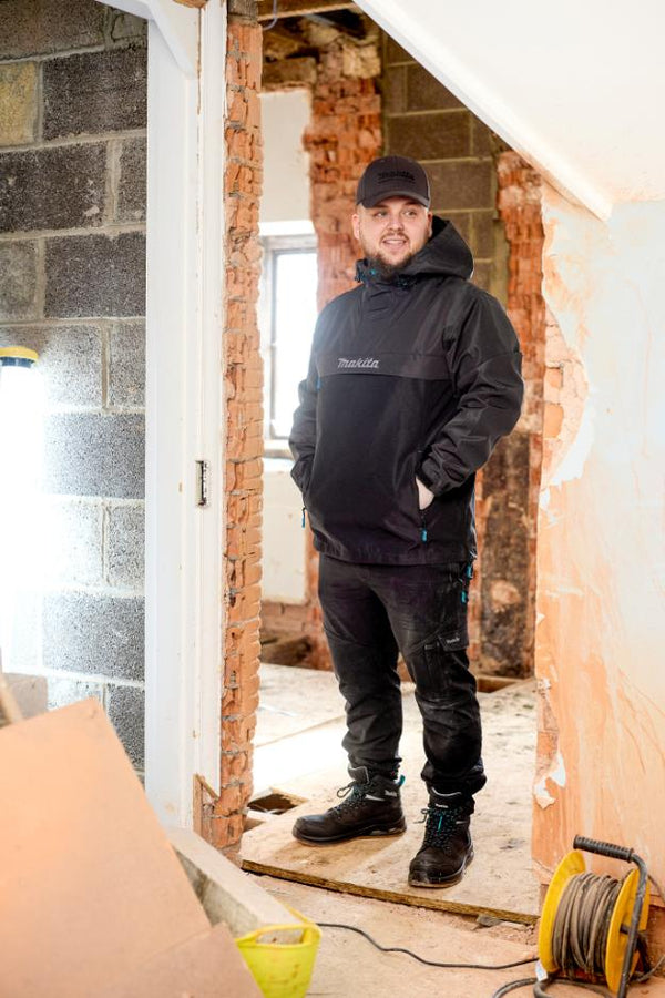 Person wearing a black jacket with a brand logo in a construction or renovation setting.