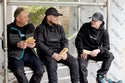 Three men in Makita workwear sitting on a platform, eating sandwiches.