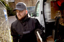builder wearing a Makita cap and jacket standing next to a van with tools inside.