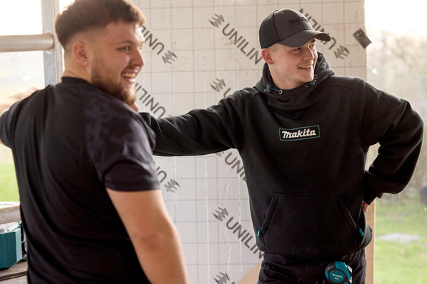 Two men in black clothing with visible Makita brand logos in an indoor setting.
