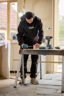 Joiner using a drill on a wooden surface with Makita tools and a Makita hoodie in the background.
