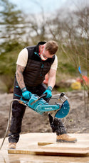 Builder using a Makita circular saw on a wooden surface outdoors wearing a Makita shield bodywarmer