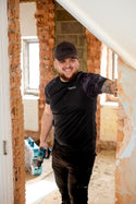 Man in a black Makita tech t-shirt and cap standing in a room under renovation with tools.