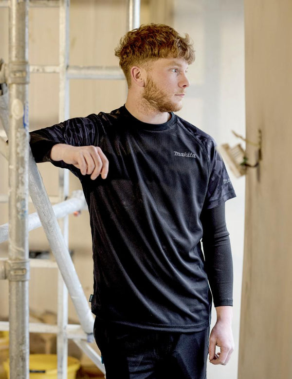 Man wearing a black Makita branded t-shirt standing indoors with a neutral background