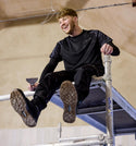 Man sitting on a metal structure wearing black  Makita workwear.