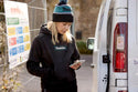 Woman wearing a black Makita womens origin hoodie with a visible Makita brand logo, standing next to a white van.