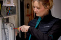 Woman in a black makita womens shield work jacket with 'Makita' branding using a screwdriver on electrical equipment.