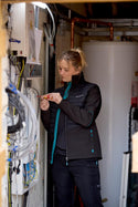Woman working on electrical wiring in a technical setting wearing a womens Makita shield work jacket
