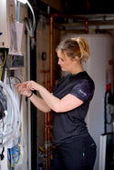 Woman in a black makita Womens t-shirt working on electrical panels in a workshop setting